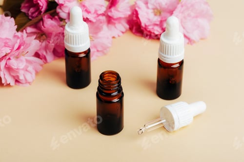 Preview: Brown glass bottles with essential oil and pink cherry blossom on beige background.