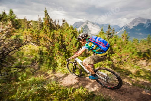 Preview: Mountain biker speeding through a trail with majestic mountains in the background.
