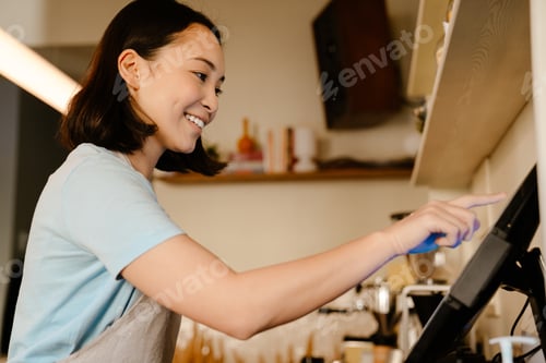 Preview: Asian barista woman smiling while working with cash register