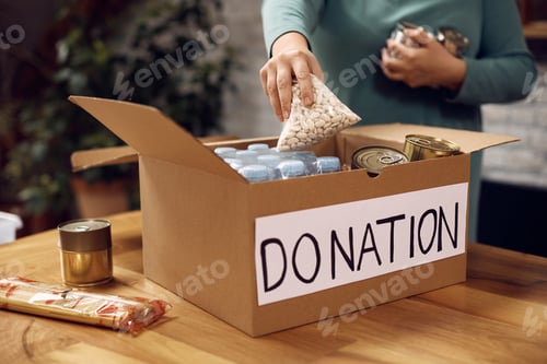 Preview: Close-up of volunteer packing food in donation box for charity food bank.