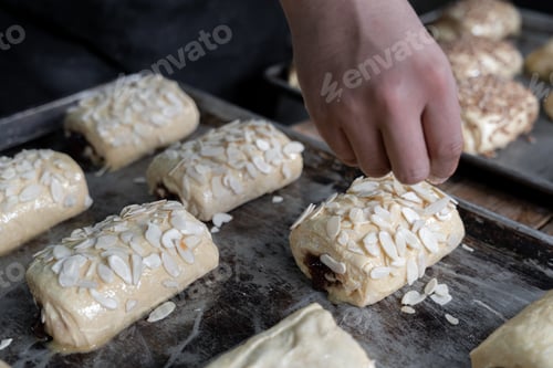 Preview: A young Hispanic baker is covering a chocolate filled bun with almond toppings