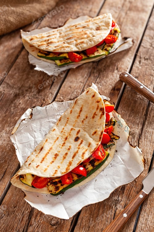 Preview: Piadina with grilled zucchini and tomatoes resting on baking paper on wooden table