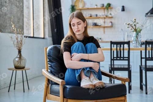 Preview: Sad stressed young woman sitting at home on armchair