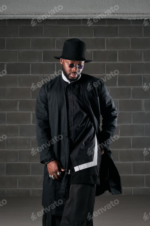 Preview: Stylish African American man in black outfit near brick wall