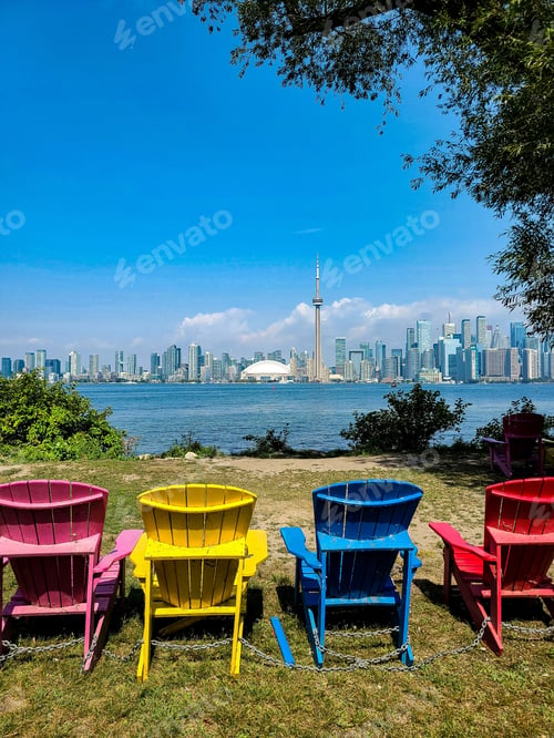 Preview: Row of brightly colored chairs in a meadow with the Toronto skyline in the background.