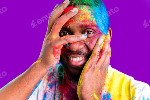 Preview: latin brazilian male in white cotton t-shirt with colorful paint of face laughing studio