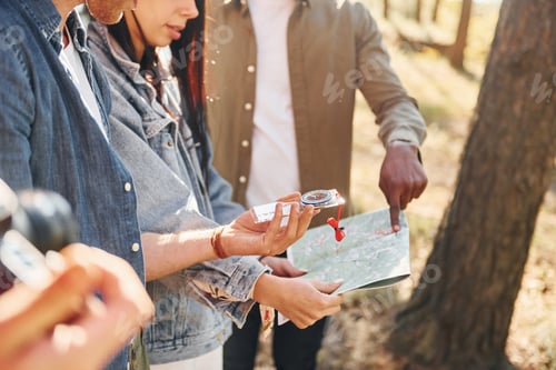 Preview: Holding map and looking for location. Group of young people is traveling together in the forest