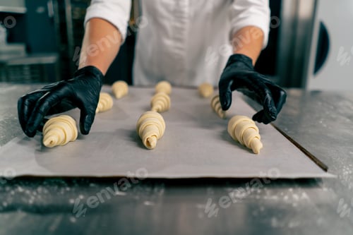 Preview: baker's hands placing shaped uncooked croissants on a baking sheet with parchment for baking in oven