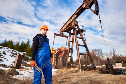 Preview: Young oil man standing in front of pump jack.