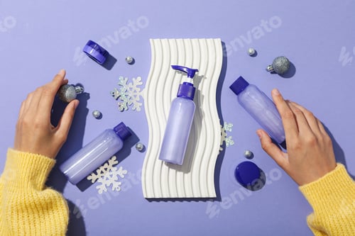 Preview: Cosmetic bottles, decorations and female hands on purple background, top view