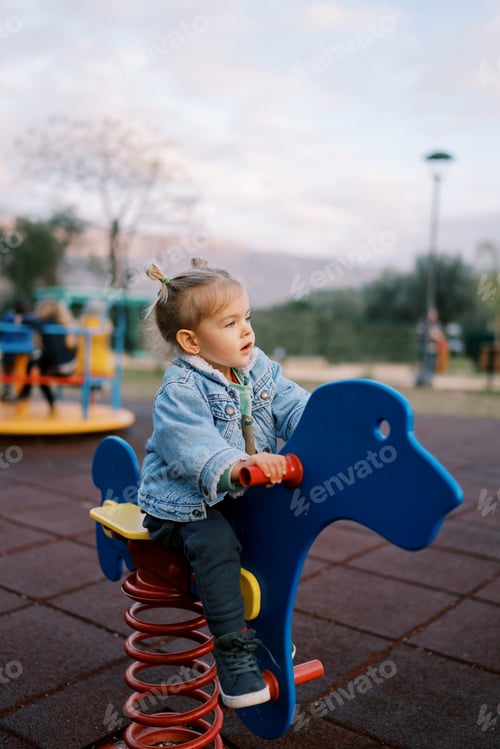 Preview: Little girl sits on a swing-spring holding the handles and looks ahead