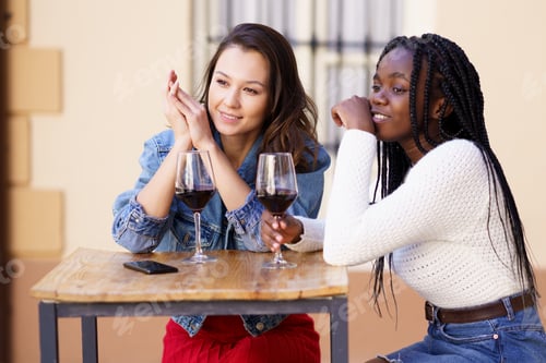 Preview: Two women drinking red wine sitting at a table outside a bar