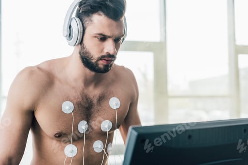 Preview: shirtless sportsman in headphones running on treadmill during endurance test in gym