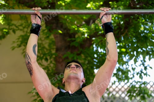 Preview: Determined athlete performing pull ups on horizontal bar during outdoor calisthenics workout
