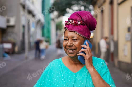 Preview: Happy senior african woman wearing traditional dress and turban while talking on smartphone call