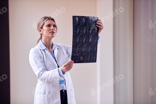 Preview: Female Doctor Wearing White Coat Standing In Hospital Corridor Looking At CT Or MRI Scan