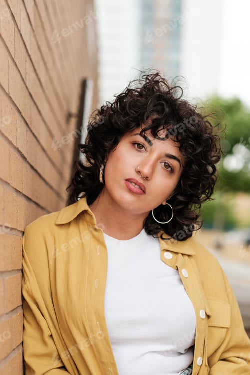 Preview: Young woman leaning against brick wall wearing yellow overshirt