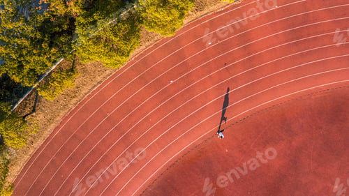 Preview: Aerial view of a person running on a running track with the sun casting a golden light on the path