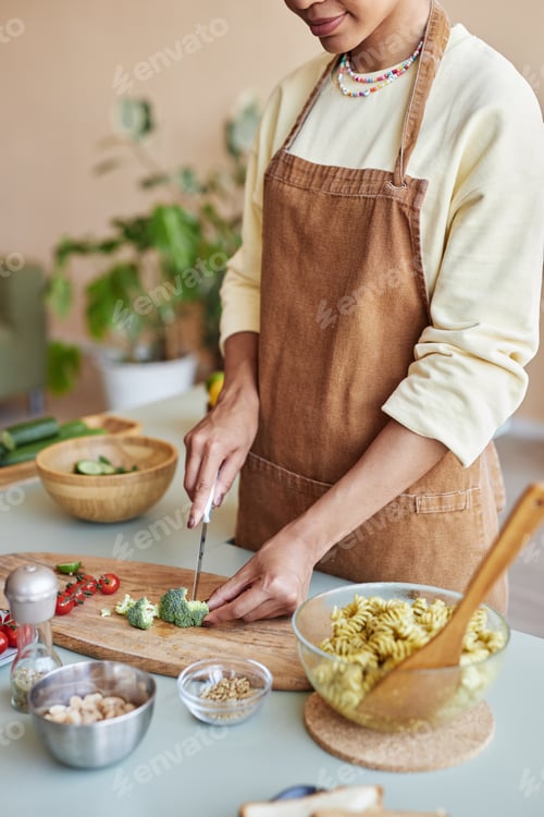 Preview: Young black woman cutting vegetables cooking pasta dish in kitchen