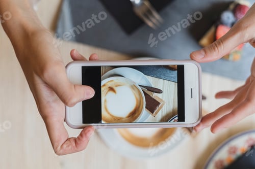 Preview: Overhead view of woman in a cafe taking cell phone picture of cappuccino
