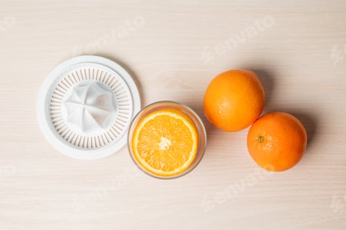 Preview: Top view of freshly cut oranges in a glass next to a juicer on a wooden surface