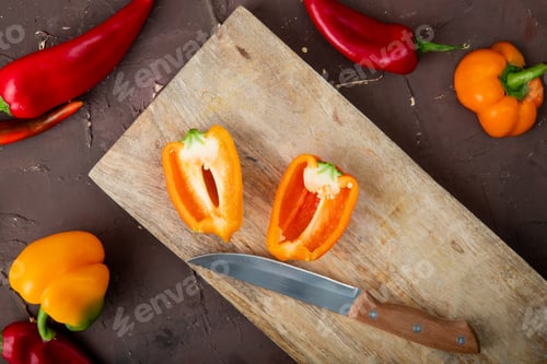 Preview: close-up view of cut pepper on wooden surface with knife and peppers on maroon background