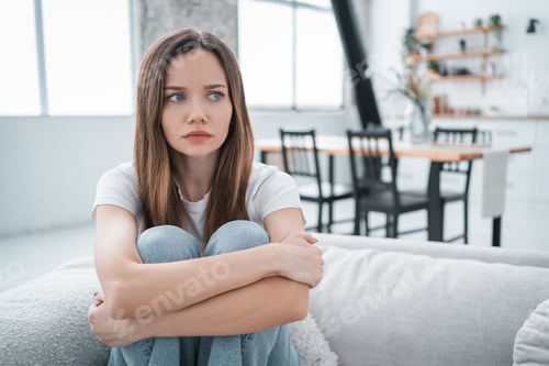 Preview: Sad Caucasian woman sitting alone hugging her knees and looking depressed.