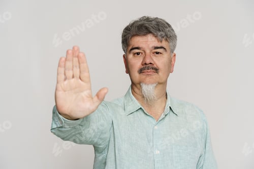 Preview: Mature man with grey beard showing stop gesture at camera