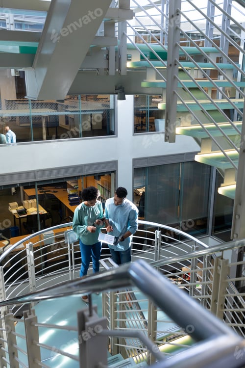 Preview: High angle view of young african american colleagues discussing over file on staircase at workplace