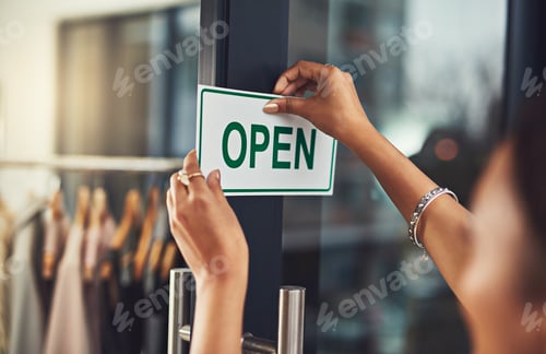 Preview: Closeup shot of a young business owner hanging up an open sign on the door of her shop