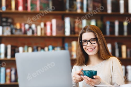 Preview: Beautiful young girl with coffee mug working on laptop and smiling