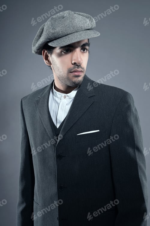 Preview: Mafia Fashion Man Wearing Grey Striped Suit With Cap. Black Hair And Brown Skin. Studio Shot.