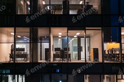 Preview: Business building with office and workspaces with desks, laptops and armchairs at night
