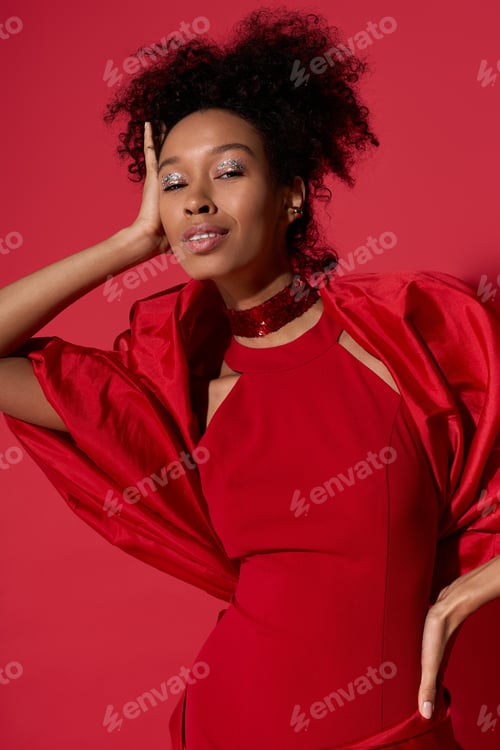 Preview: Radiant young woman in striking red outfit exuding confidence and charm against vibrant background