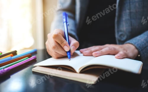 Preview: Closeup image of a woman writing on a blank notebook with colored pens on the table