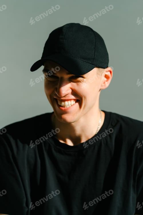 Preview: Portrait of stylish handsome caucasian man fashion model in t shirt and cap, studio shot.