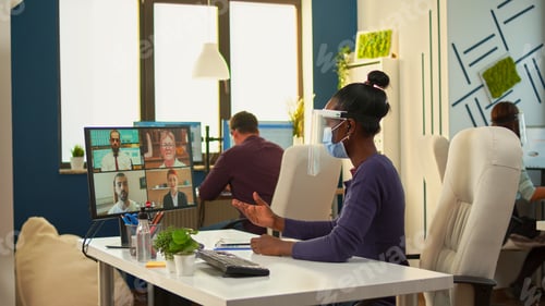 Preview: African worker with face mask talking on videocall in office room