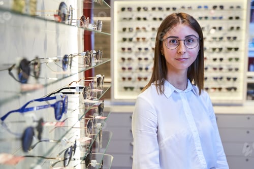 Preview: Beautiful young woman in glasses standing in optical store