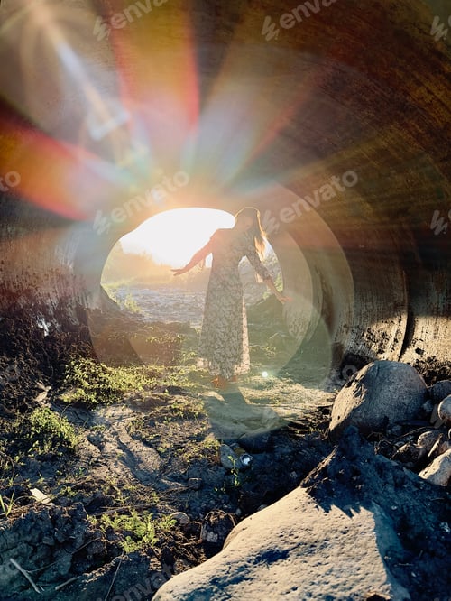 Preview: a girl in a long dress is illuminated by the sun in a tunnel