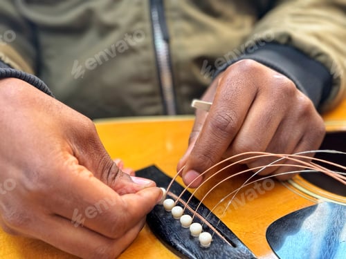 Preview: A black diverse unrecognizable guitarist male musician replaces strings on an acoustic guitar