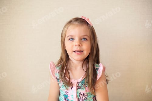 Preview: Close up of cute adorable smiling little girl with blue eyes against beige wall indoors