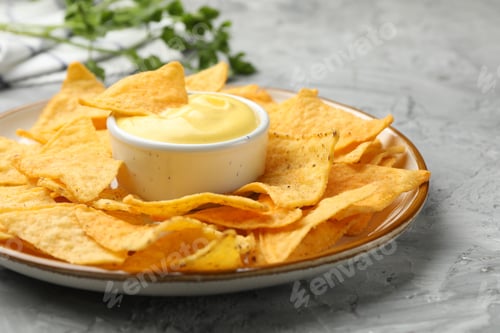Preview: Tasty cheese dipping sauce in bowl, nacho chips and parsley on grey table, closeup