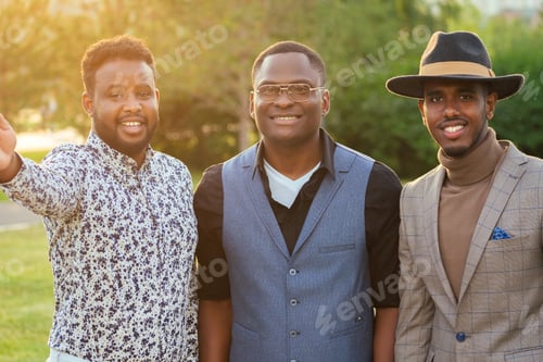 Preview: a group of three black men in stylish suits in a summer park.