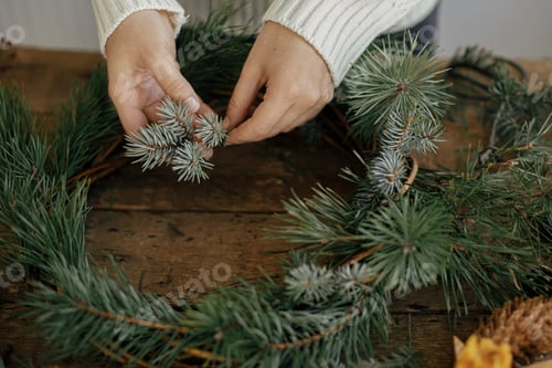 Preview: Hands holding fir branch and arranging christmas wreath on rustic background. Winter Workshop