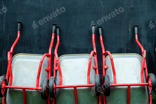 Preview: Array of red wheelbarrows lined up against a dark textured wall
