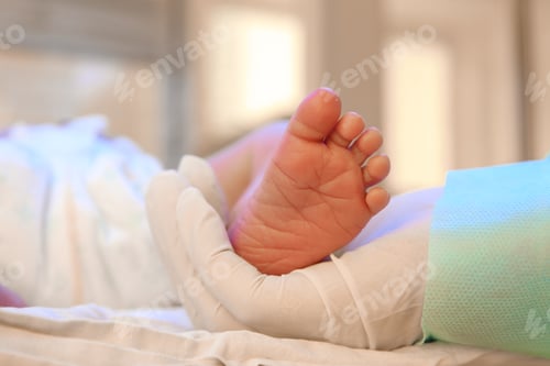 Preview: Doctor holding newborn child's foot in hospital, closeup