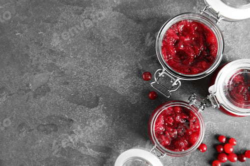 Preview: Jars with tasty cranberry sauce on grey background, flat lay. Space for text