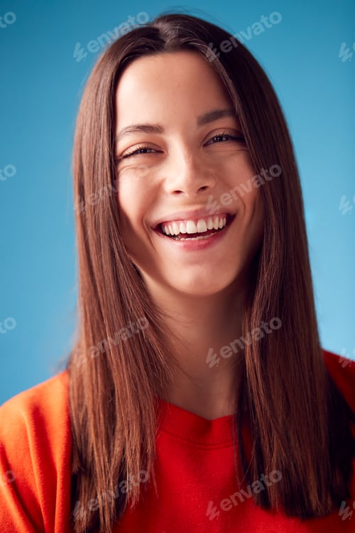 Preview: Studio Portrait Of Confident Young Woman Looking Into Camera Against Blue Background