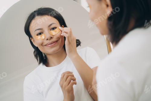 Preview: Smiling female apply under eye patches, looking at mirror. Skincare treatment routine, self-care
