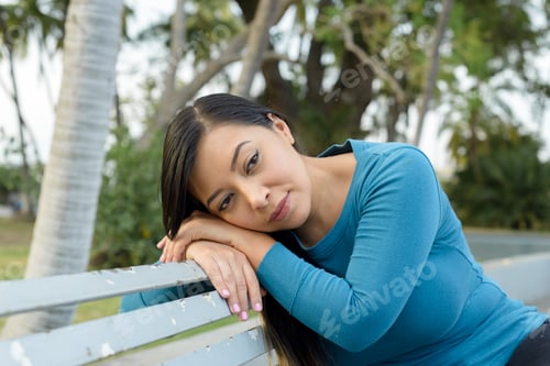 Preview: Woman sitting on a bench in the park with a bored expression.
